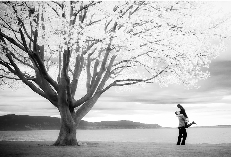 artsy engagement session picture with tree and ocean in the background infrared effect Missy and Chase romp on the beach